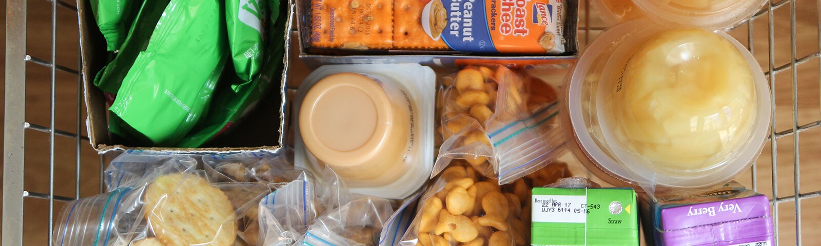 Basket full of snacks like applesauce, juice boxes, fruit cups and crackers