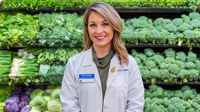 Image of a Registered Dietitian standing in front of shelf of leafy green vegetables Image of a Registered Dietitian standing in front of shelf of leafy green vegetables